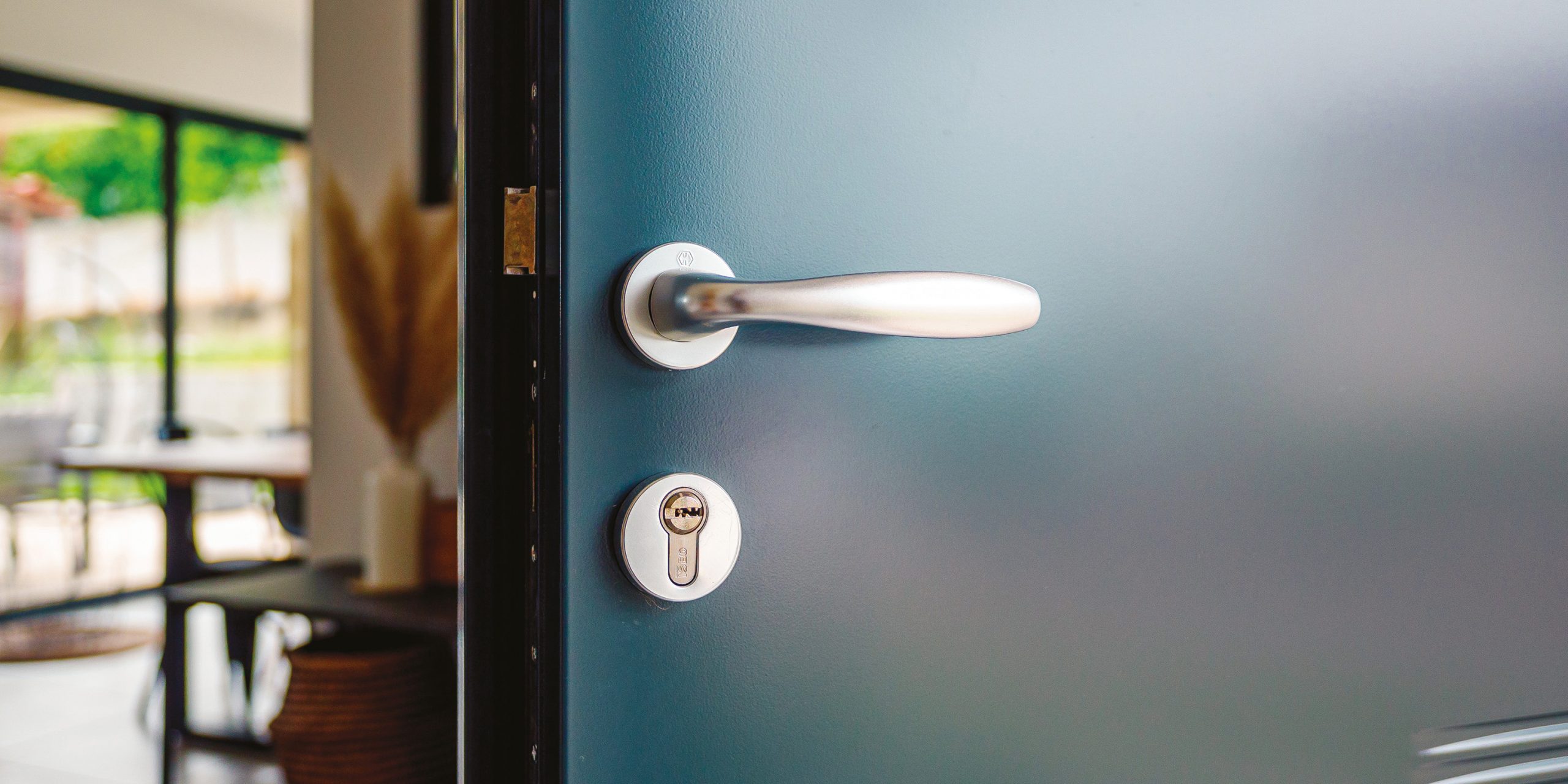 Zoom sur la poignée et serrure d'une porte d'entrée entrouverte sur un salon lumineux